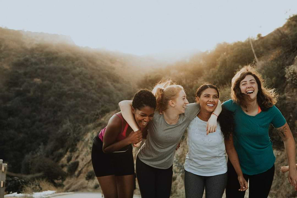 Four women hugging and smiling outdoors with a scenic background